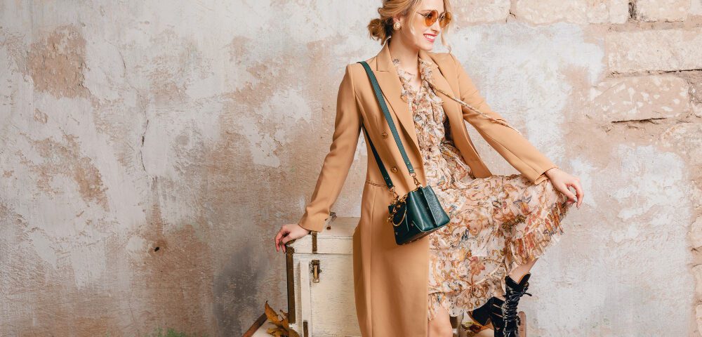 attractive stylish blonde woman beige coat sitting suitcases against wall street